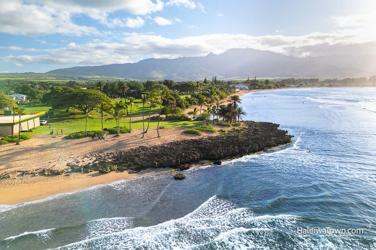 aerial view of alii beach park rocky shore, sandy beach and green lush park full of trees
