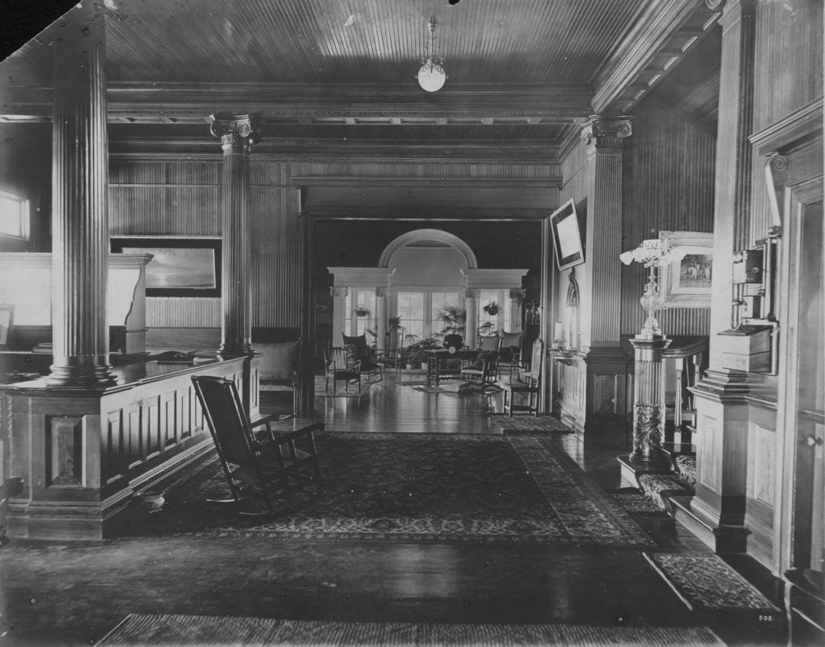 interior of the historic Haleiwa hotel with the front desk on the left a spacious seating area in front and wood paneling on the walls and arches in the entrances