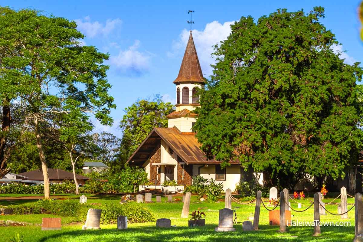 Liliuokalani church building with a tall tower in a grassy field with cemetery and tall tress around it