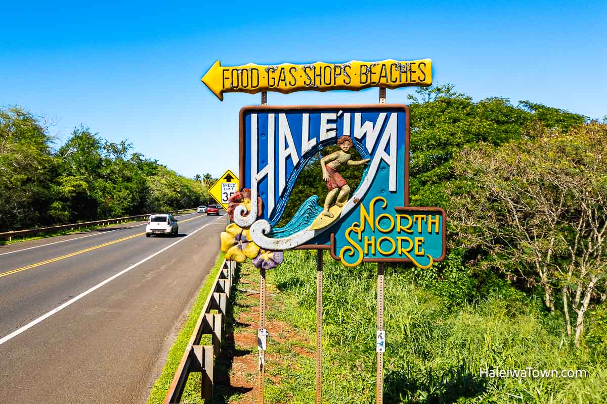 large sign of a surfer riding a wave surrounded by the words north shore and haleiwa with an arrow pointing to the town's food gas shops beaches