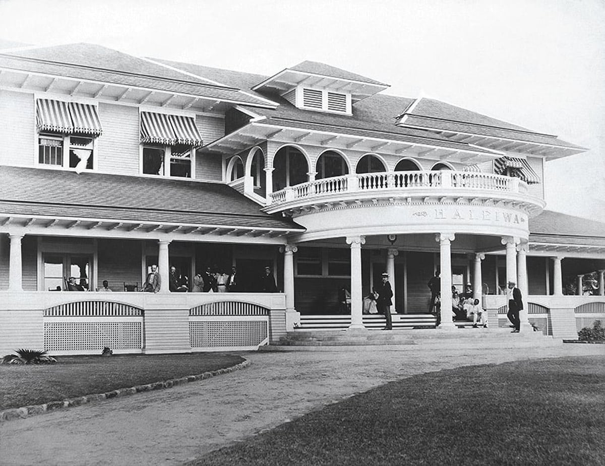 side view of large two story-victorian-style hotel for Haleiwa with a round deck on the top floor and men inside and out