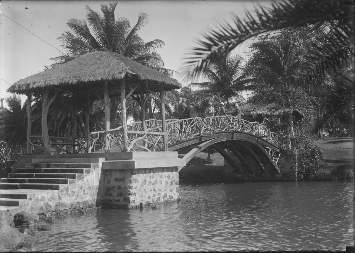 historic bridge with intricate wood railings over the anahulu stream with men walking through it and palm tree around it