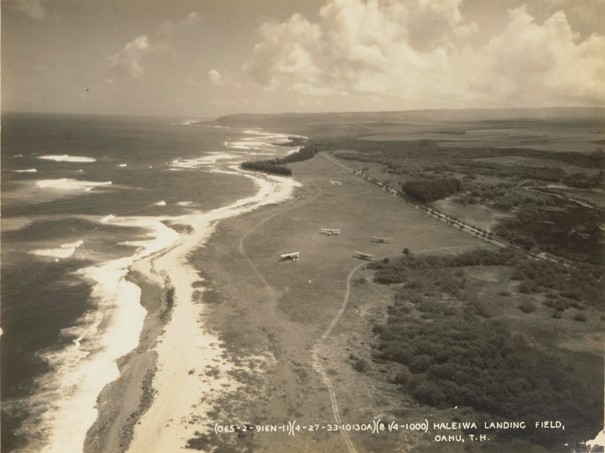 historic aerial view of airport landing by the beach shore with old planes parked on the grass in 1933