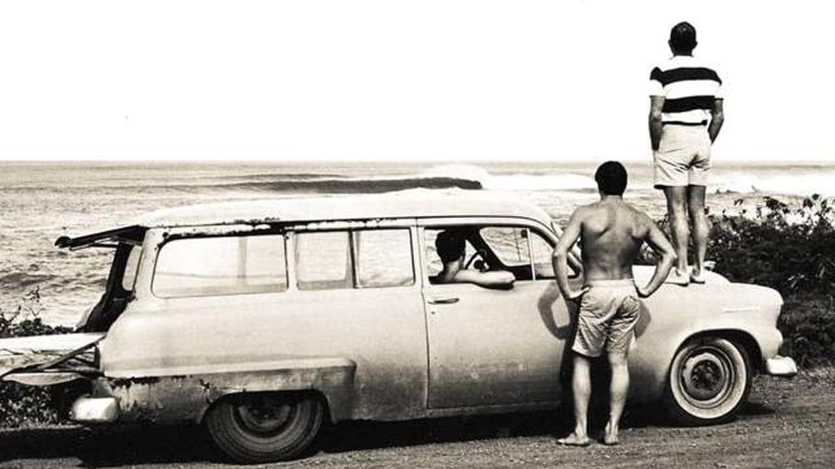 black and white historic view of surfers watching the waves from the beach and inside a car on the north shore