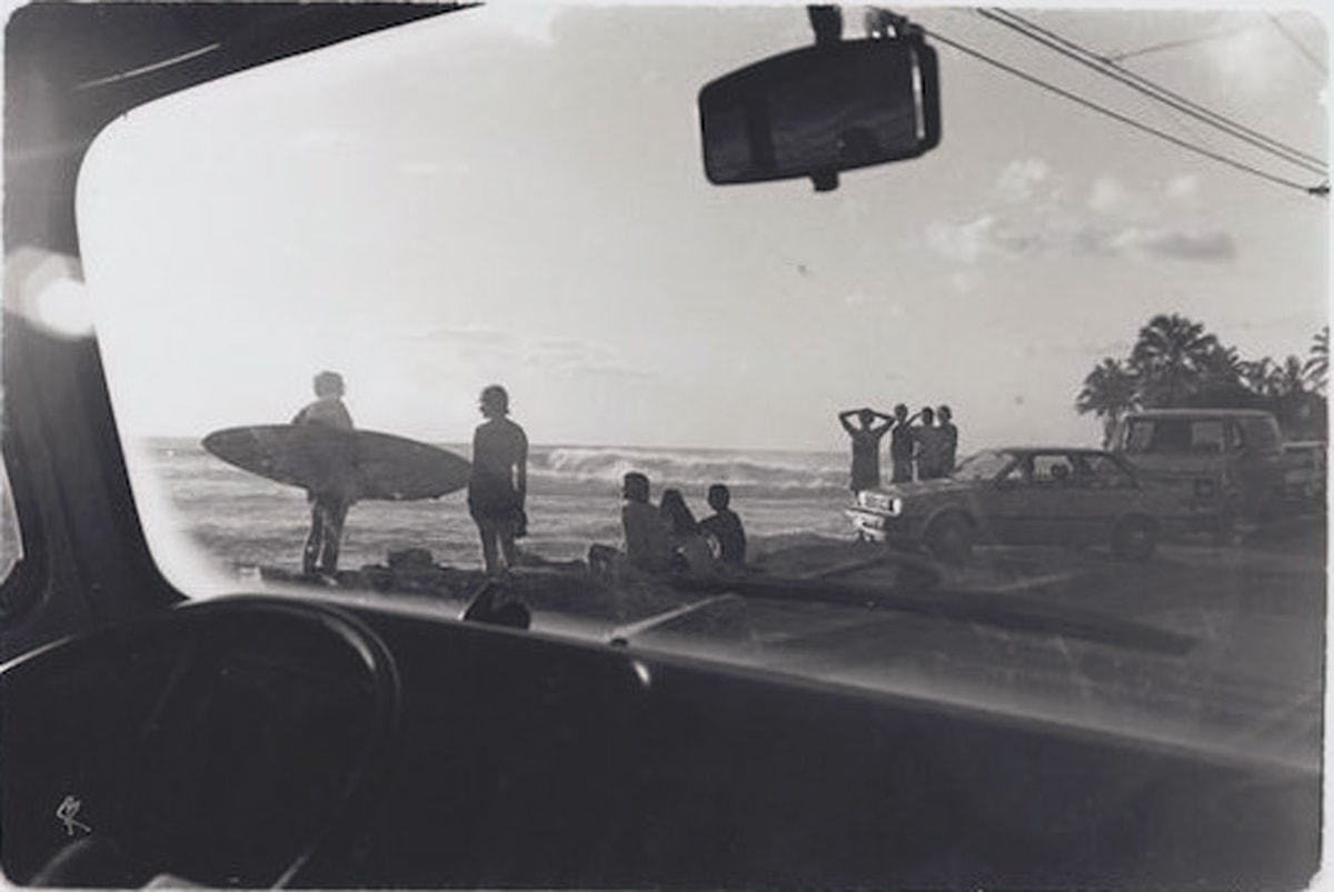 black and white historic view of surfers watching the waves from the beach and inside the cars at sunset beach