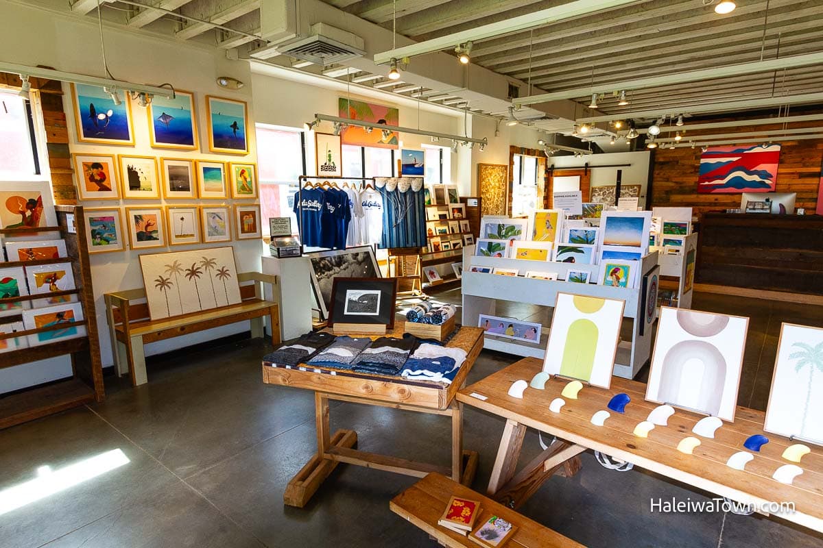 numerous paintings with an ocean theme hanging on the wall and on shelves inside the store Polu Gallery