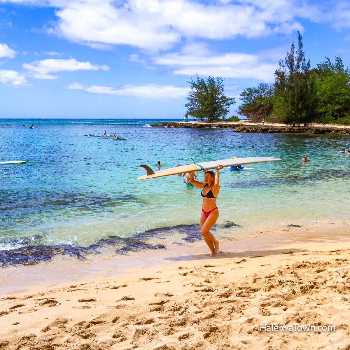 girl carrying a surfboard over her head on north shore oahu beach
