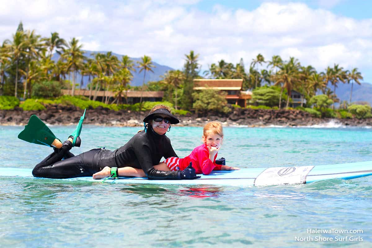 women with a child laying  on a surfboard in the ocean