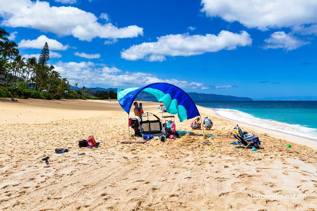Calm summer conditions at Ehukai Beach Park with wide sandy beach and families relaxing