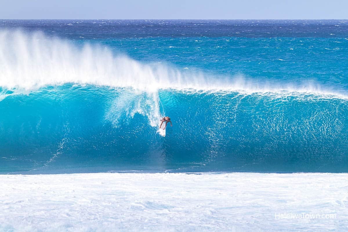 surfer dropping on big wave at pipeline