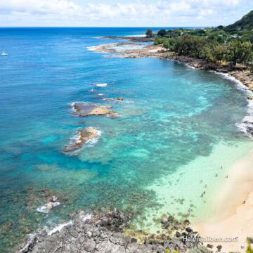 Aerial view of Three Tables Beach on Oahu's North Shore with clear turquoise water, reef, and people snorkeling near shore.