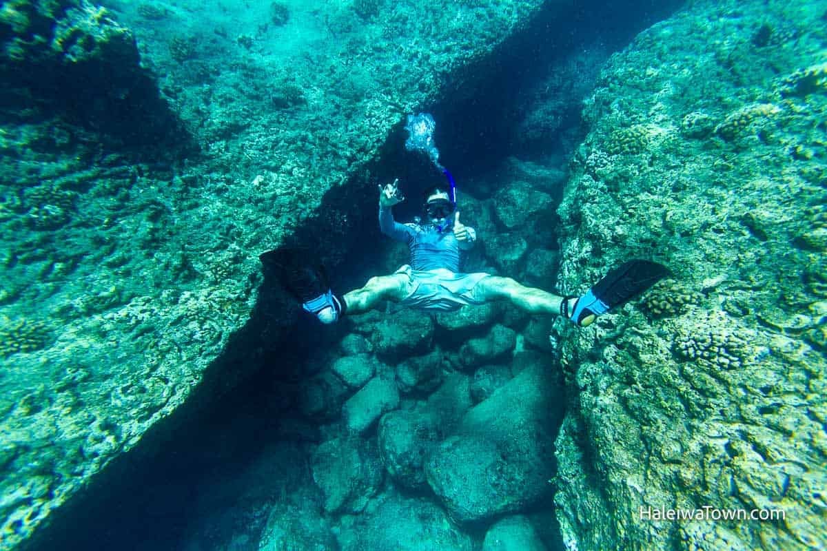 Snorkeler swimming through an underwater crevice in the reef at Pipeline.